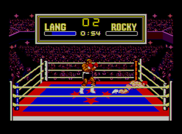 Captura de Rocky. Vemos a dos luchadores sobre un ring que parece estar en el centro de un gran estadio. A la derecha Rocky y a la izquierda Lang. El luchador de la derecha está tendido en el suelo. En la parte superior se ve un marcador con el tiempo y la vida de los luchadores. La barra de vida de la derecha está vacía.